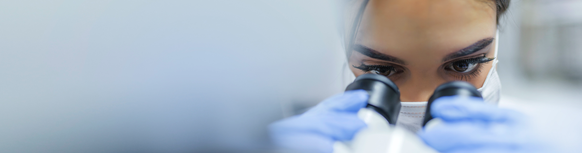 masked woman looking into a microscope